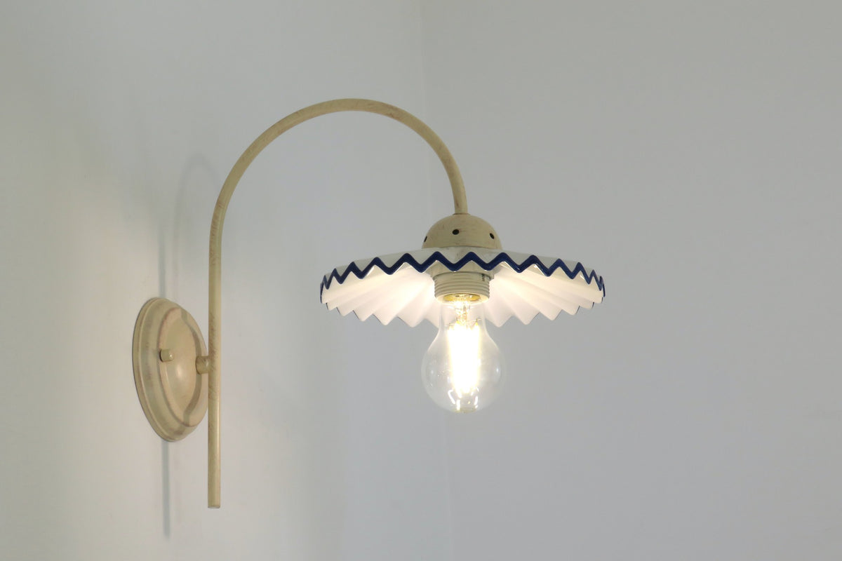 Applique BERENICE avorio accesa: luce calda sotto il paralume in ceramica ondulata bordo blu – Diamantlux